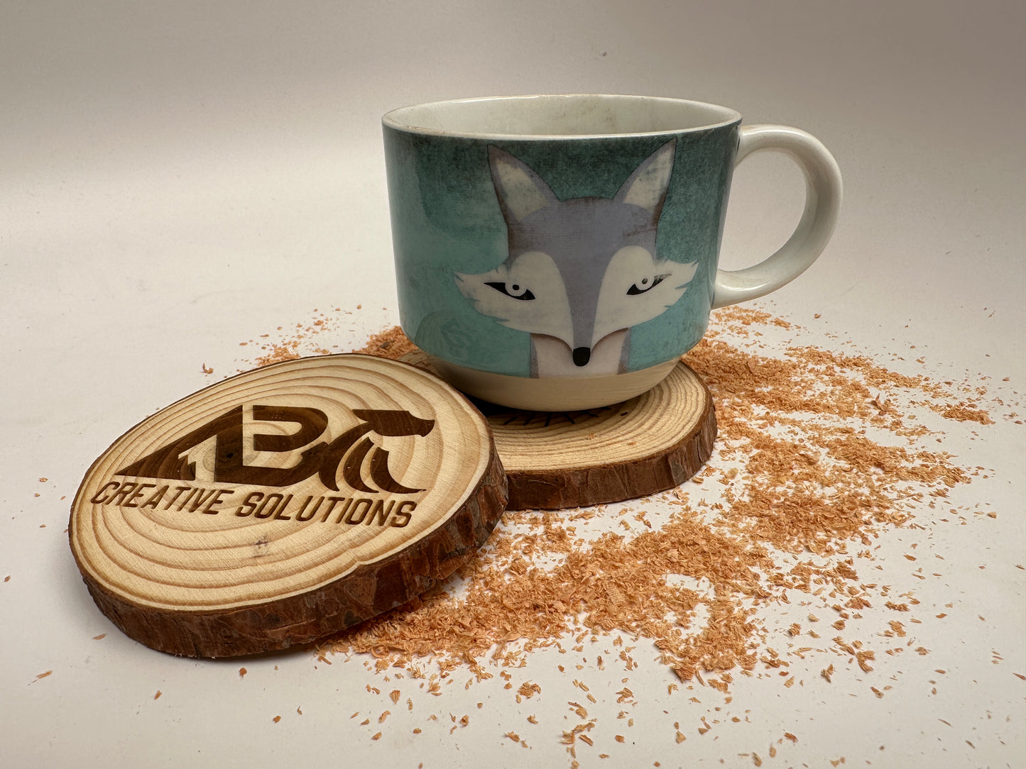 Wooden coaster with a coffee cup on top and a second coaster engraved with the ABC Creative Solutions logo